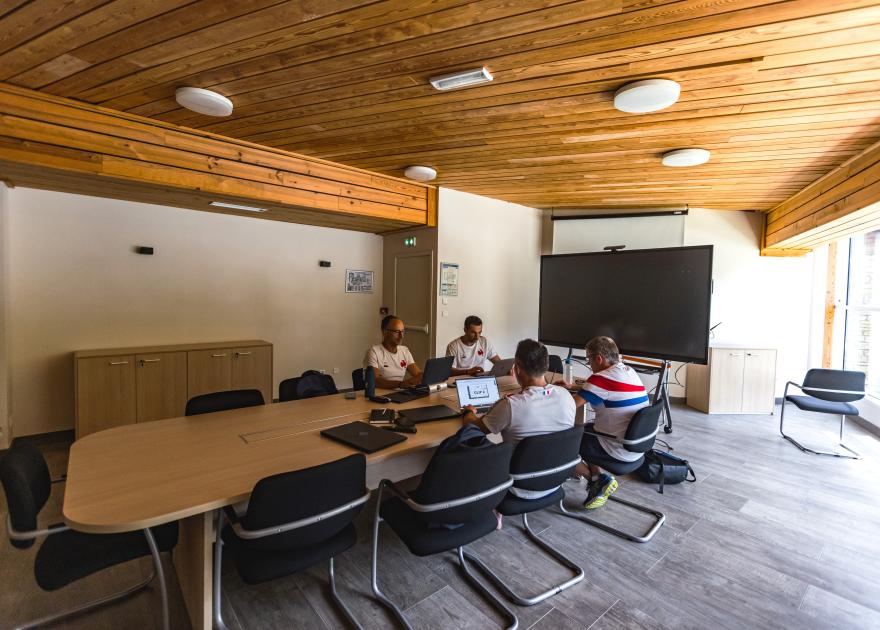 Salle de réunion de 70 m² au centre Balnéa (Loudenvielle), aménagée autour d’une grande table ovale pouvant accueillir une quinzaine de personnes, équipée d’un écran interactif tactile avec visio-conférence, d’un paperboard, d’une connexion internet, et baignée de lumière naturelle grâce à ses larges baies vitrées.